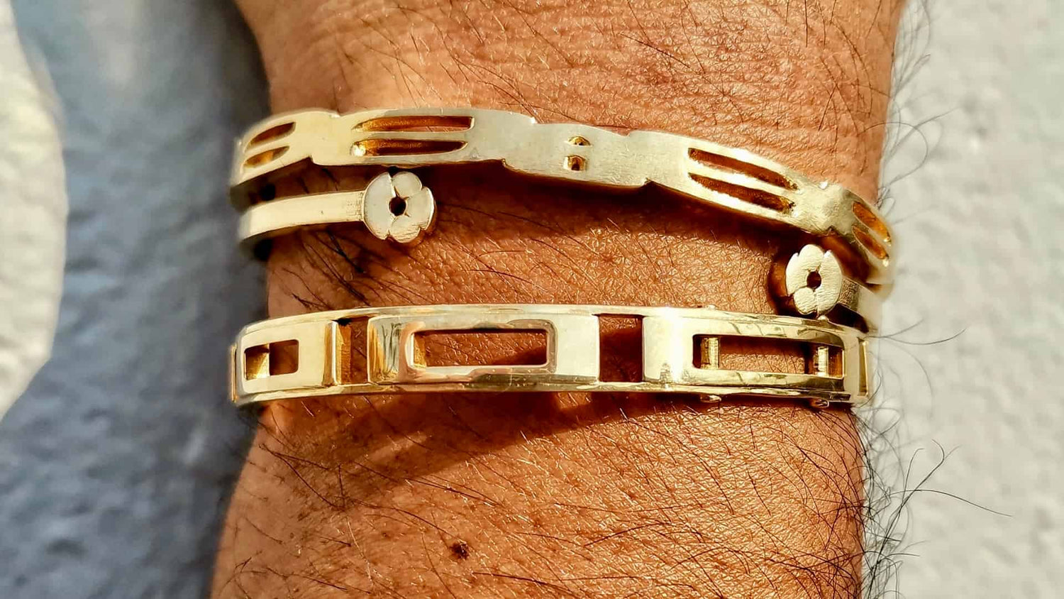 Tres pulseras de oro de diseño geométrico, colocadas en la muñeca de una persona, capturadas con luz natural que resalta sus acabados y texturas.